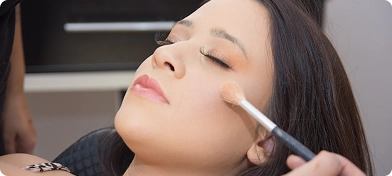 Bir güzellik salonunda profesyonel bir makyaj sanatçısı, genç bir kadının yanaklarına fırçayla allık sürüyor.