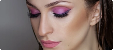 Yoğun pembe göz farı, uzun siyah eyeliner ve mat pembe ruj içeren çarpıcı makyajı olan genç bir kadının yakın çekim fotoğrafı.