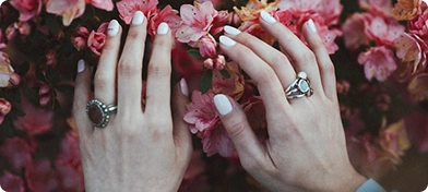 Beyaz ojeli tırnakları ve yüzükleri olan bir kadının ellerinin, yoğun pembe çiçeklere dokunuşunun yakın çekim görüntüsü; doğal güzellik ve bahar teması.