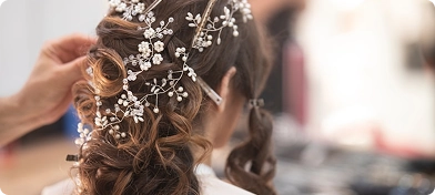 Profesyonel bir kuaförün, bir kadının özenle hazırlanmış gelin saçı veya özel gün topuzuna zarif kristal ve inci saç tokaları eklerken çekilmiş yakın plan görüntüsü.